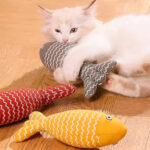 A cat enjoying playtime with a grey striped plush fish toy.